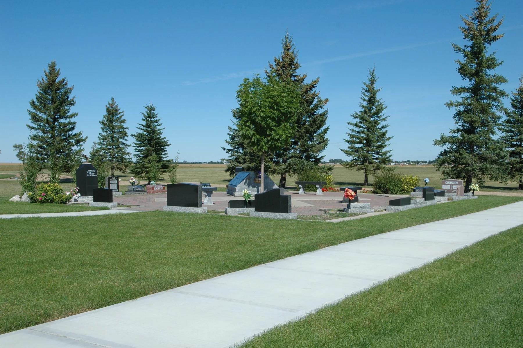 Sunlit lawns, evergreen trees and memorials beneath a blue sky at Sunset Cemetery.