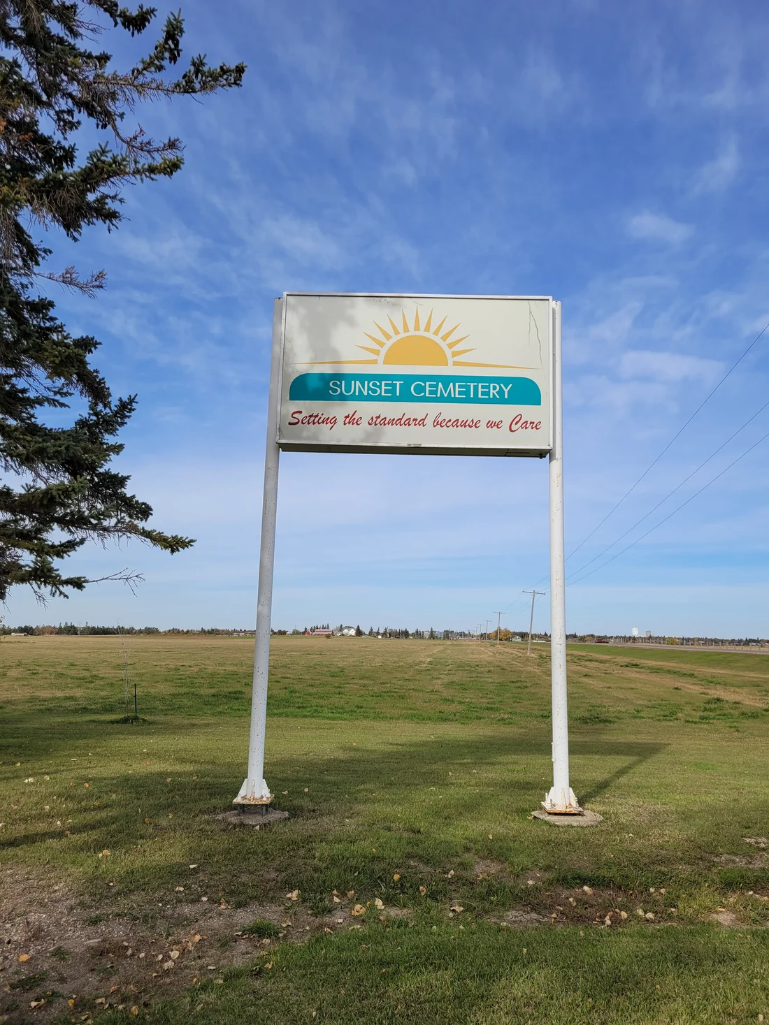 Sunset Cemetery roadside sign and sun logo against a bright blue sky.